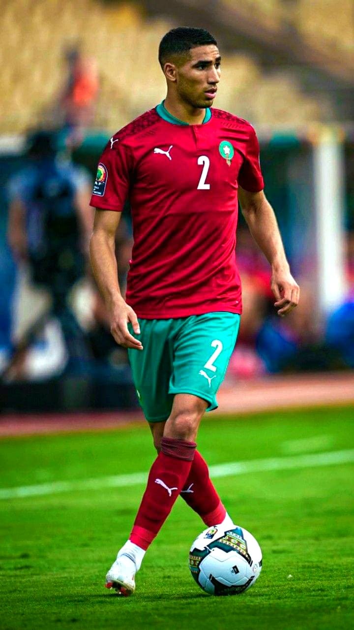 A soccer player in a red and green uniform with the number 2 controls the ball on a grass field during a match, as fans across the world tune in through IPTV Latvia to catch every exciting moment.