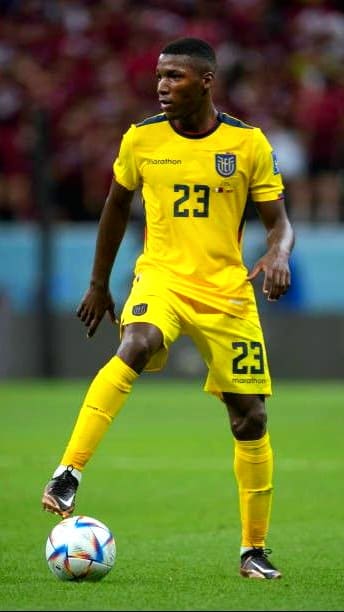 A soccer player in a yellow Ecuador national team uniform with number 23 controls a ball on the field during a match, as fans around the world follow the action through IPTV Latvia.